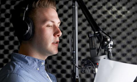 Voice actor reading in front of a microphone in a sound studio.