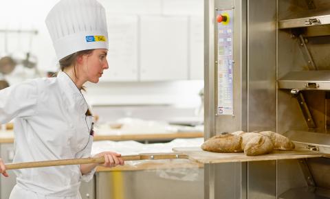 Culinary student takes bread out of the oven.